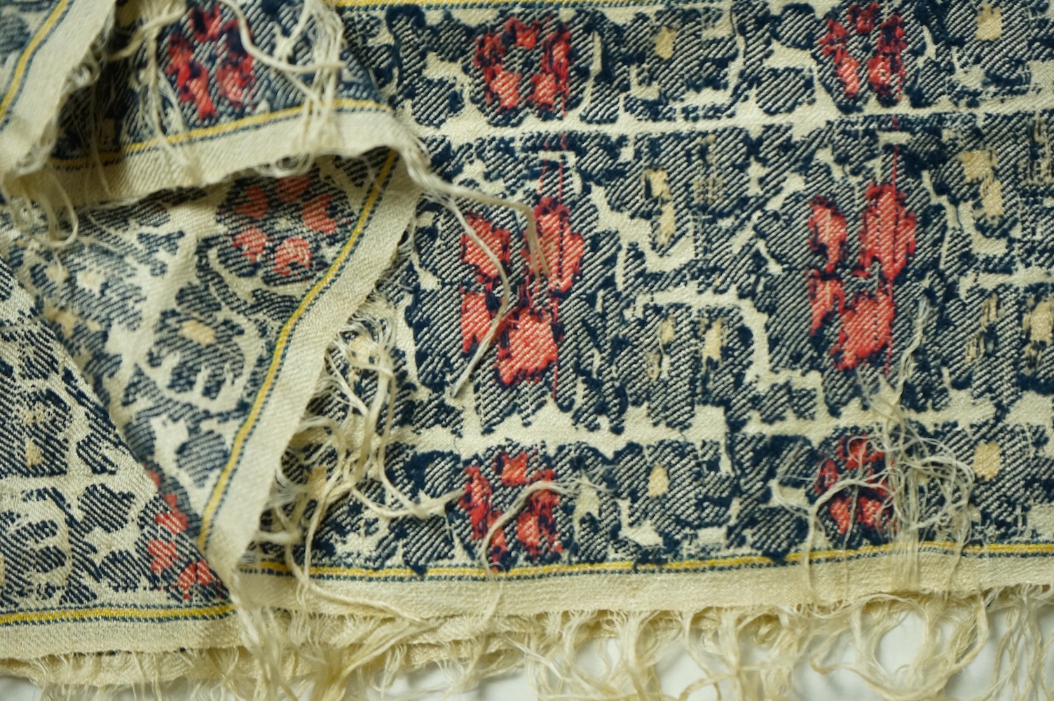 A 19th century silk woven shawl. Woven with a cream silk ground, with indigo, red and yellow, floral stylistic Buta motifs and bordered with three rows of a similar floral vining pattern. The edges fringed. 148cm x 152cm